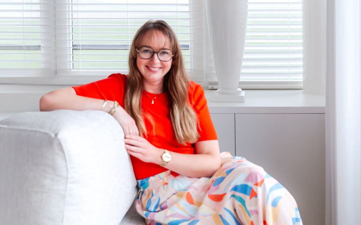 Jonge vrouw met lang haar, een bril en een rood shirt zittend op een bank