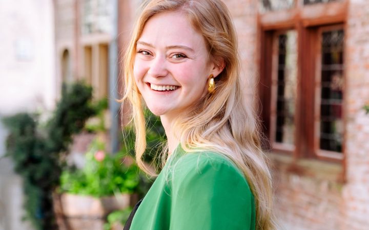 Jonge vrouw in donkere jurk en groen jasje.