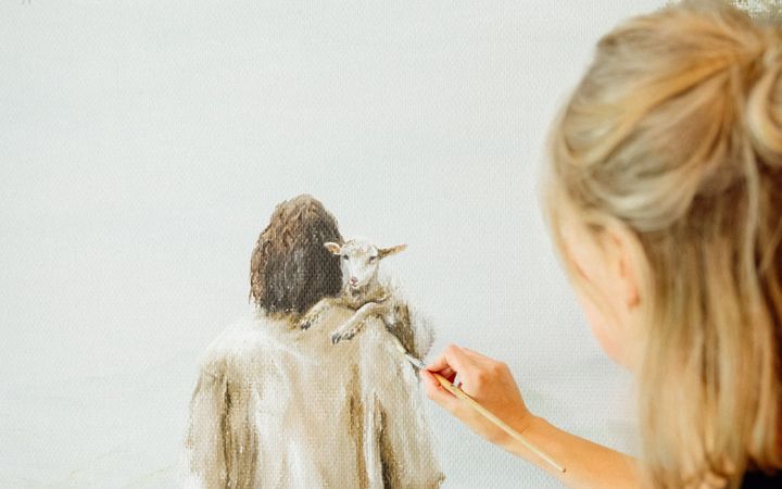 Een vrouw schildert op een muur een herder met een lam op de schouder.