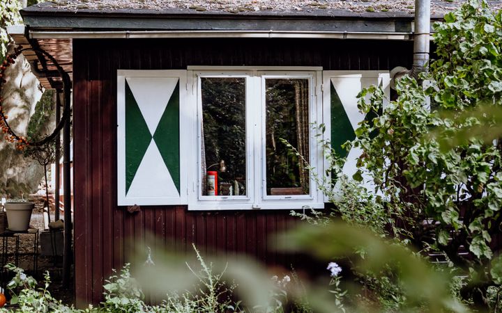 Het boshuisje is gemaakt van donker hout en heeft ramen die voorzien zijn van grote luiken.