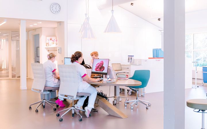 Verpleegkundigen in witte kleding achter een bureau met computers.