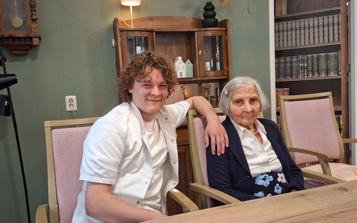 Jonge, mannelijke verpleegkundige zit naast een oudere cliënte in woonzorgcentrum Maranatha. 