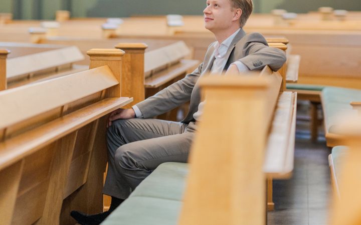 Jongeman met blond haar, gekleed in een licht pak, zittend in een kerkbank.