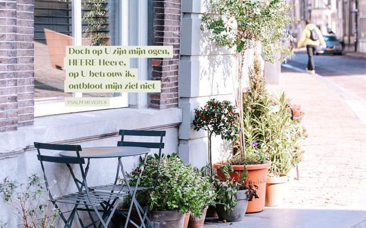 Een tafeltje met twee stoeltjes en daarnaast planten op een stoep, met eroverheen de tekst uit Psalm 141 vers 8: „Doch op U zijn mijn ogen, HEERE Heere, op U betrouw ik, ontbloot mijn ziel niet.”