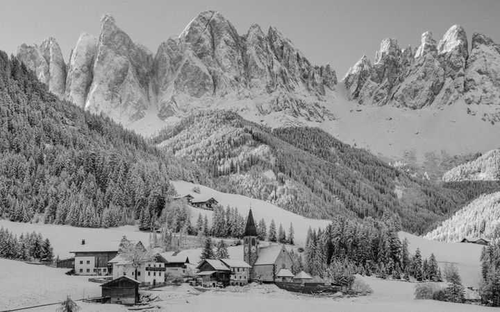 Zwart-witfoto van besneeuwde bergen, met enkele huisjes en een kerk in het dal 