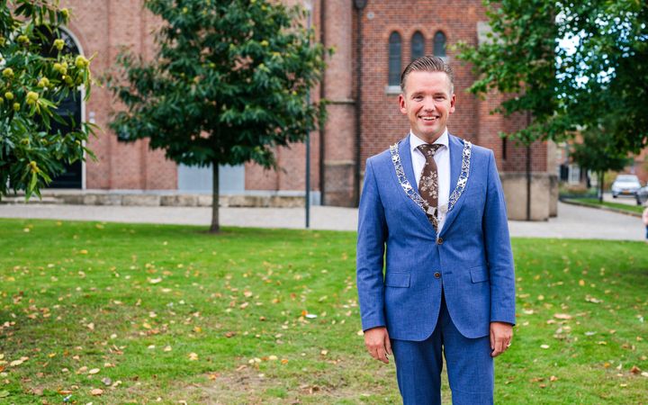Burgemeester Jurgen van Houdt, met ambsketen om, voor de eeuwenoude Schildkerk in het centrum van Rijssen.