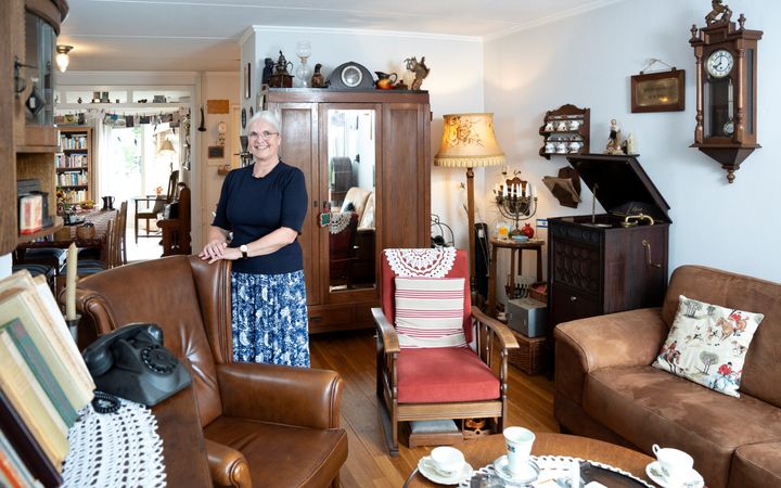 Oudere vrouw in een woonkamer vol met oude spulletjes. 