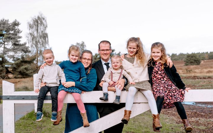 Echtpaar met vijf jonge kinderen achter een wit hek in de natuur.