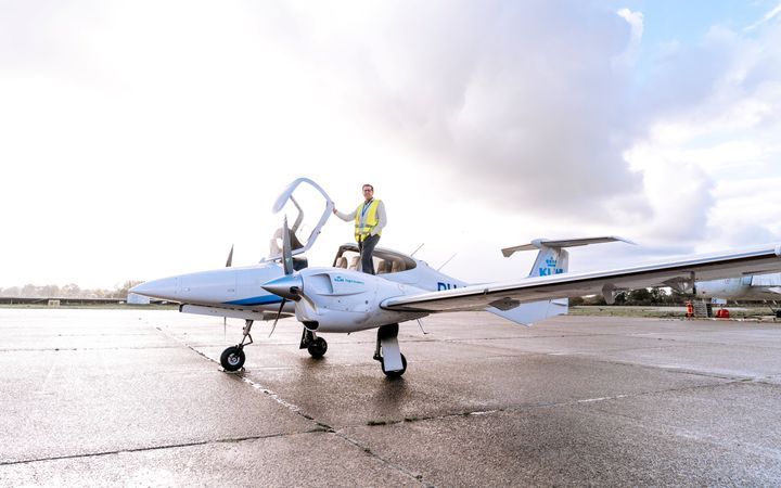 Man met bril en geel hesje, staande in een klein vliegtuigje met opengeslagen koepel