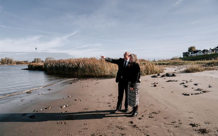 Stemmig gekleed echtpaar op een strandje bij een rivier.