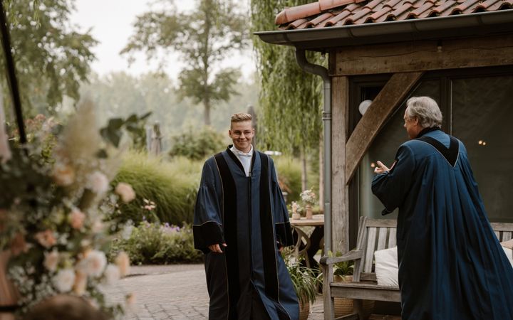 Man van middelbare leeftijd in toga verwelkomt jonge man in toga.