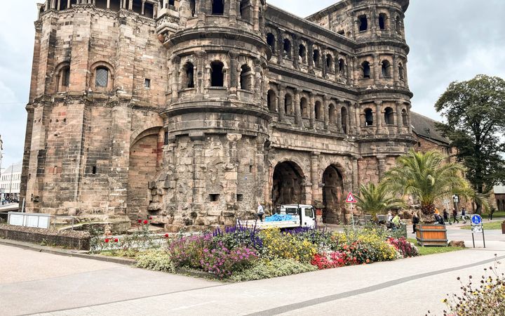 Kolossaal poortgebouw met twee poorten; ervoor een border met bloemen.