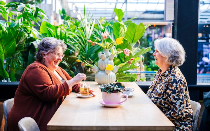 Twee vrouwen van middelbare leeftijd zitten aan een tafel, met koffie en thee.