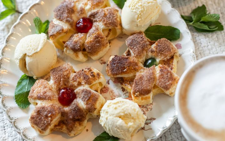 Wit bord met daarom drie bolletjes ijs, gedecoreerd met muntblaadjes, en drie bloemvormige bladerdeegpakketjes met een geconfijte kers als bloemhart.