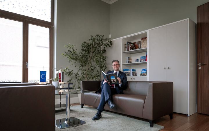 Man in donkerblauw pak, zittend op een bruine bank.