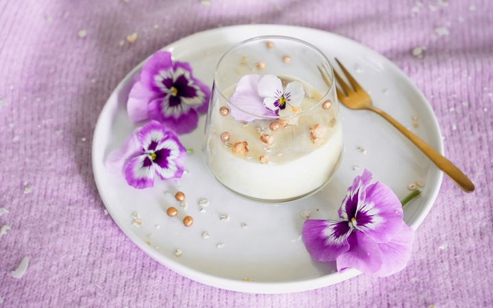Glas met een toetje op een schotel met roze bloemblaadjes.