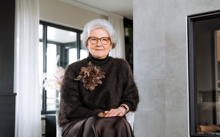 Vrouw met grijs haar, bruine bril en bruine rok en trui.