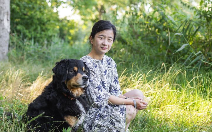 Vrouw met zwart haar en blauw-witte jurk, zittend naast een zwarte hond op het gras. Beeld Willemiene Smits.