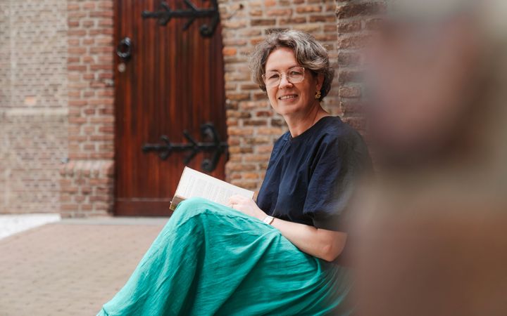 Vrouw met groene rok en blauw shirt, zittend op een stoep voor een oude kerk.
