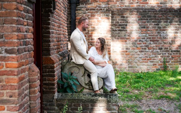 Jonge man en vrouw, zittend op een stenen bank tegen de muur van een kerk.
