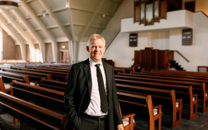 Man van middelbare leeftijd in zwart kostuum in een kerk.